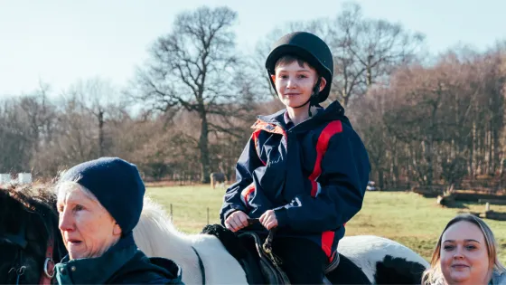 A boy rides a horse led by two women.