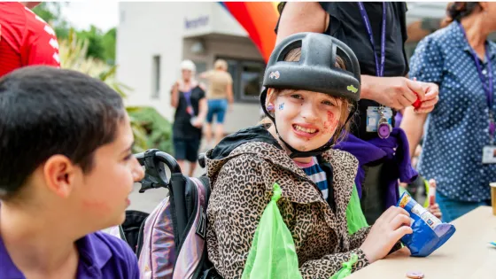A young girl wearing a helmet sits painting at a festival with her piers.